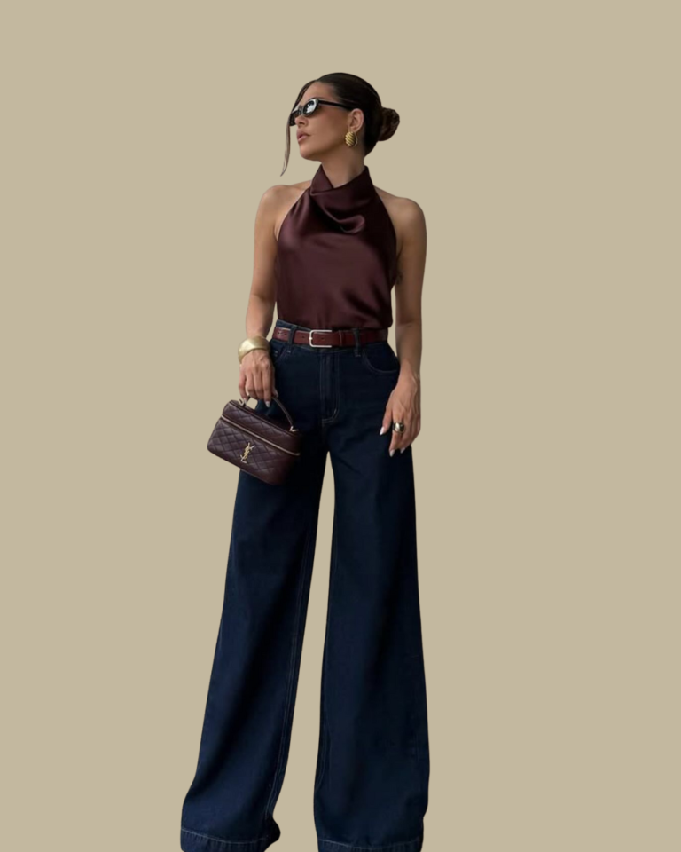 Woman with her hair in a ponytail, wearing a brown chocolate halter top, high-waisted light-wash wide-leg jeans, a wide dark brown belt, and a large brown suede shoulder bag.
